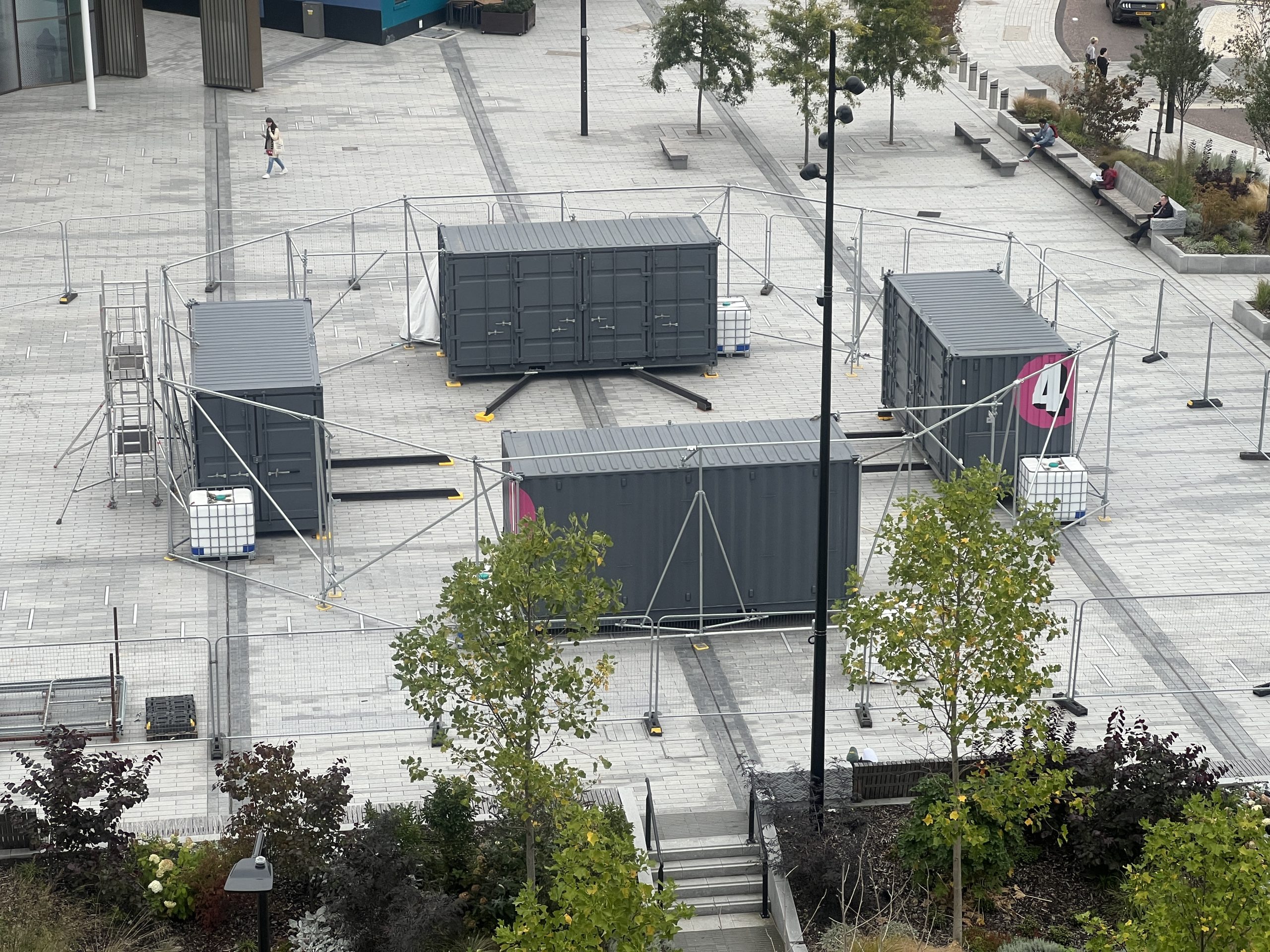 A photograph of the MET being installed at University Square. 4 20 foot high cube shipping containers are arranged in a circle surrounded by a scaffolding frame.
