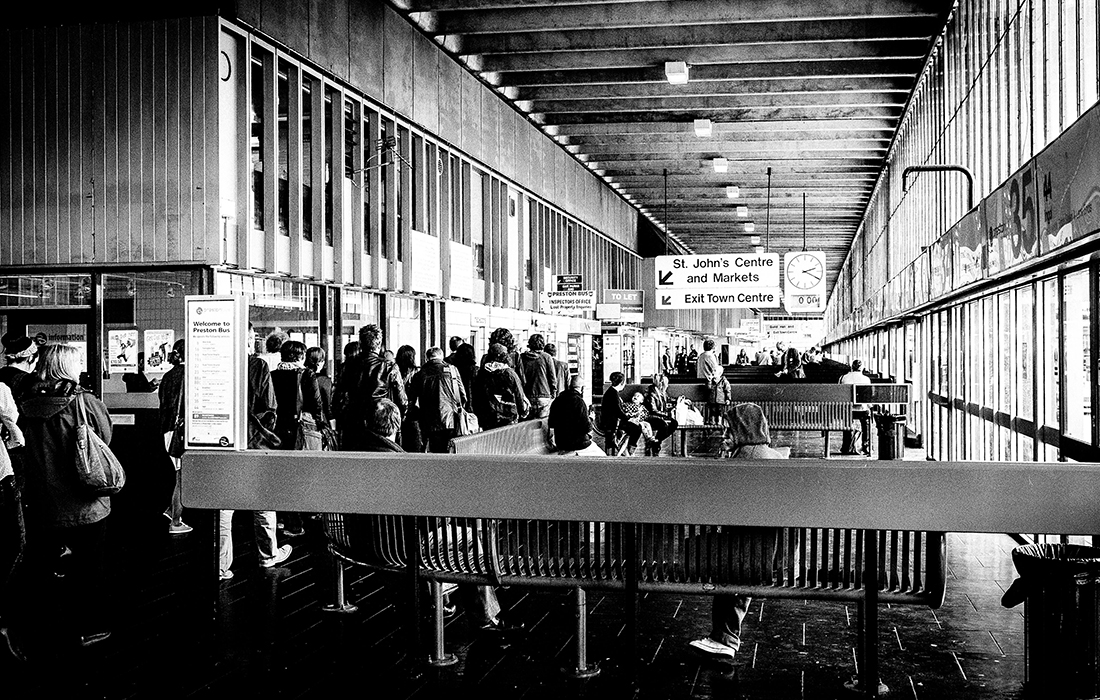 Black and white photograph of a tour group walking along the inside concourse of Preston Bus Station.