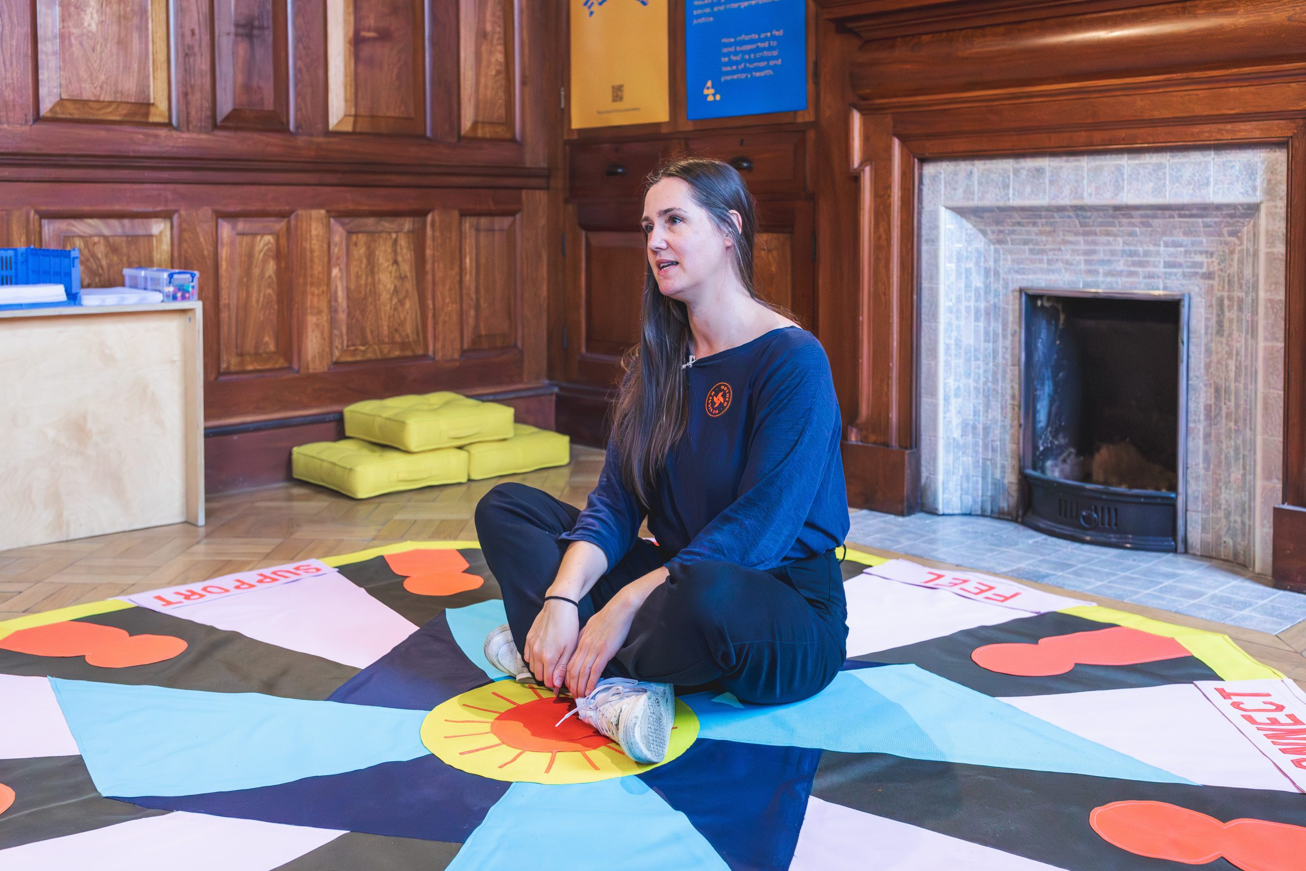White woman sitting cross-legged on a brightly coloured rug.