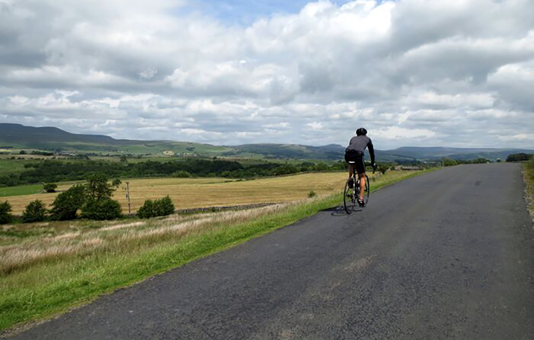 a man cycles on a road through countryside.