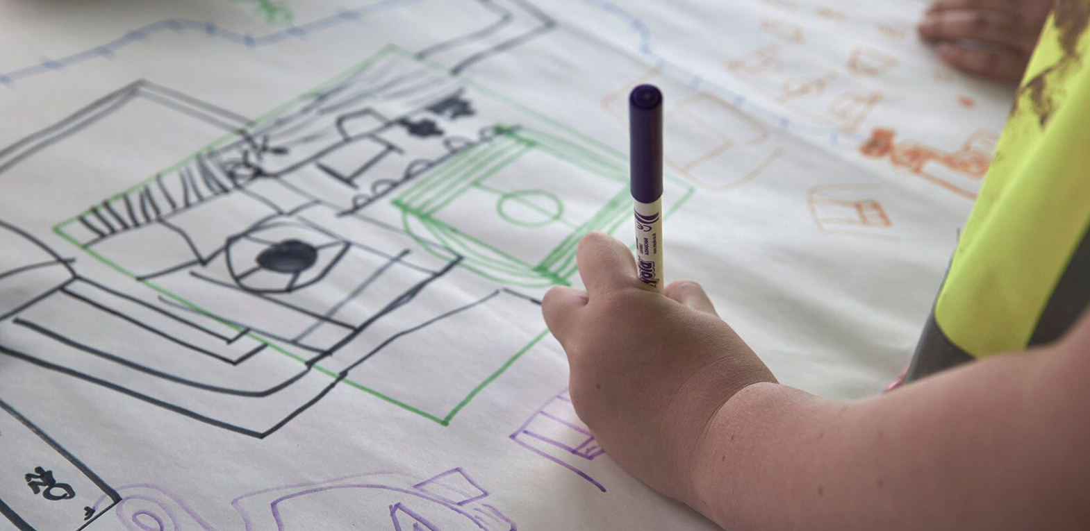 A child in hi-vis draws a plan on a large piece of paper for what their ideal home and village could look like