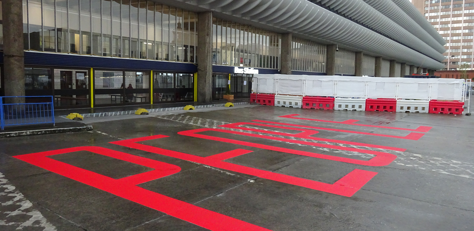 'People' artwork by LOW PROFILE. The word people is painted in road marking paint on the forecourt of Preston Bus Station.
