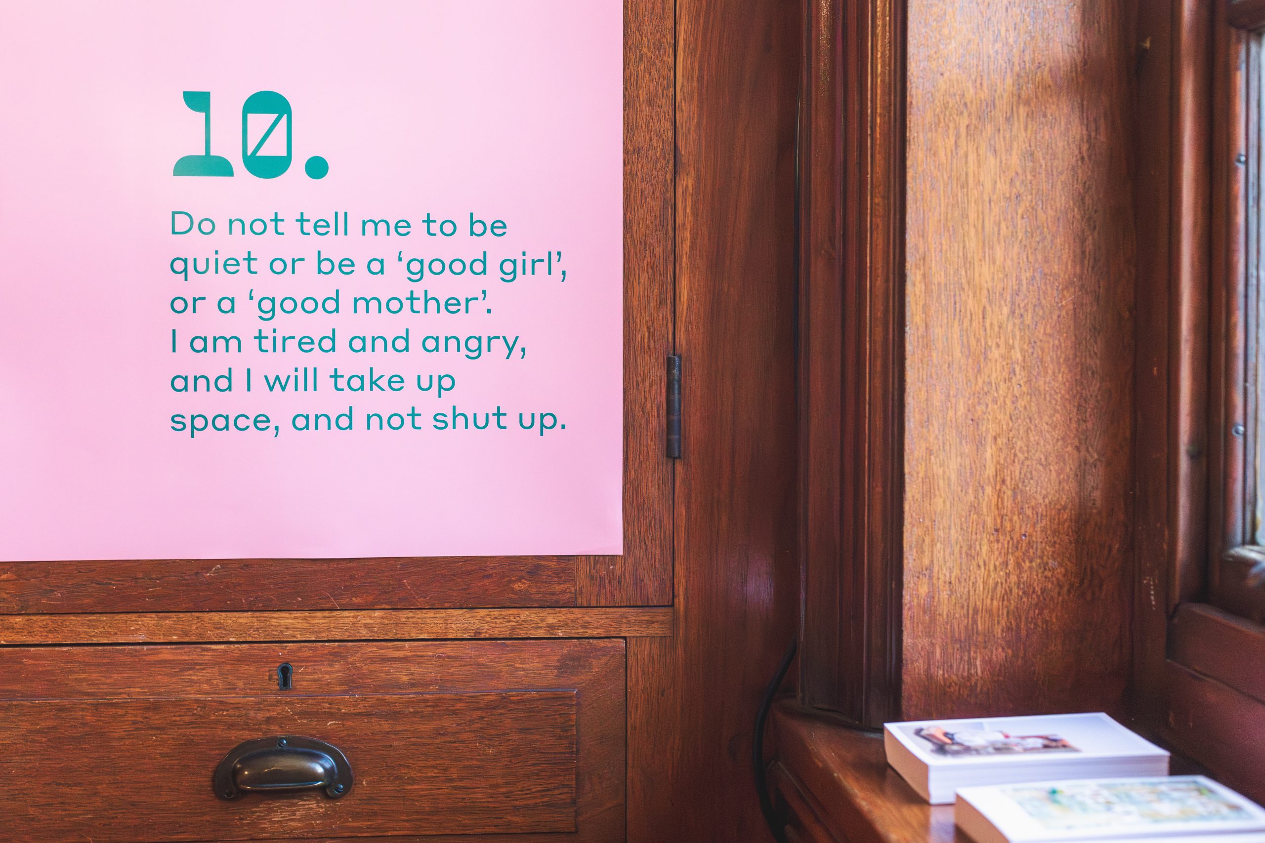 Corner of pink poster on a wooden cupboard, with the words 'Do not tell me to be quiet or be a 'good girl', or a 'good mother'. I am tired and angry, and I will take up space, and not shut up.